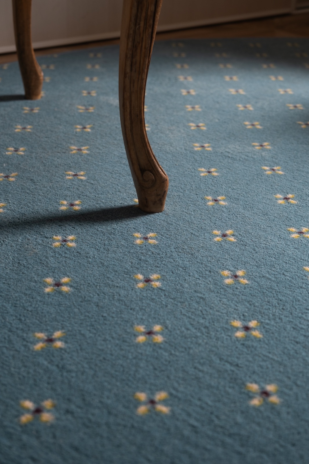 Détail de la moquette bleue à fleurettes, sous un pied de chaise d'époque