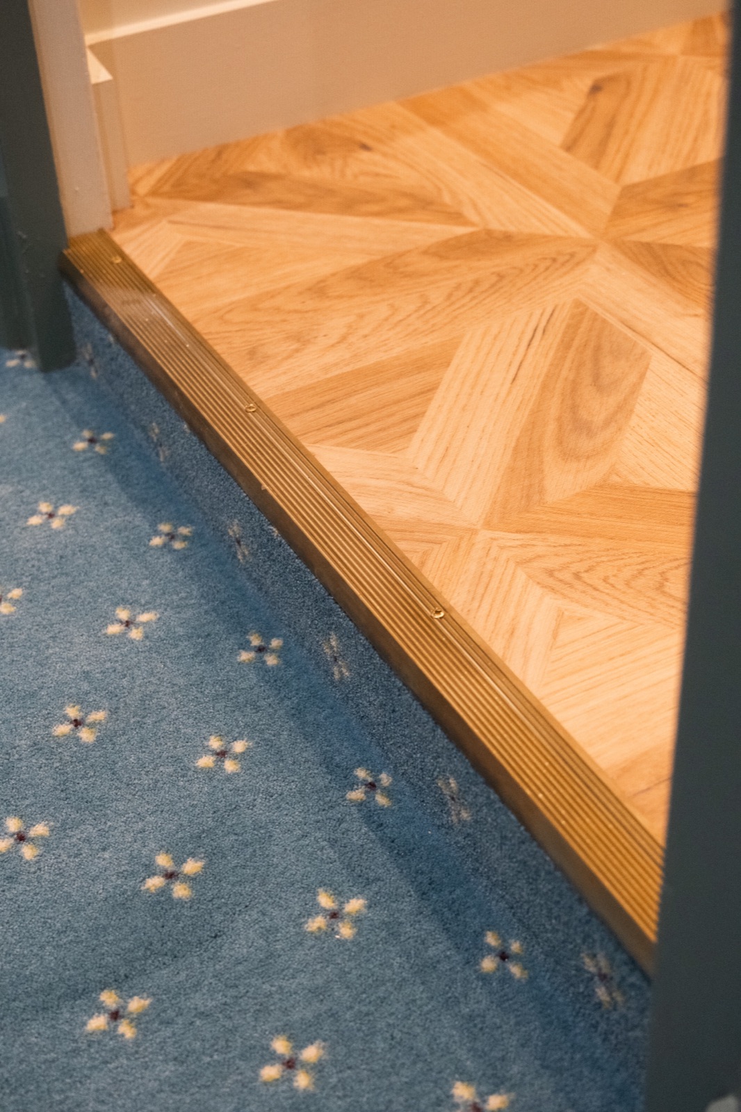 Transition entre moquette de chambre et parquet géométrique, profilé laiton