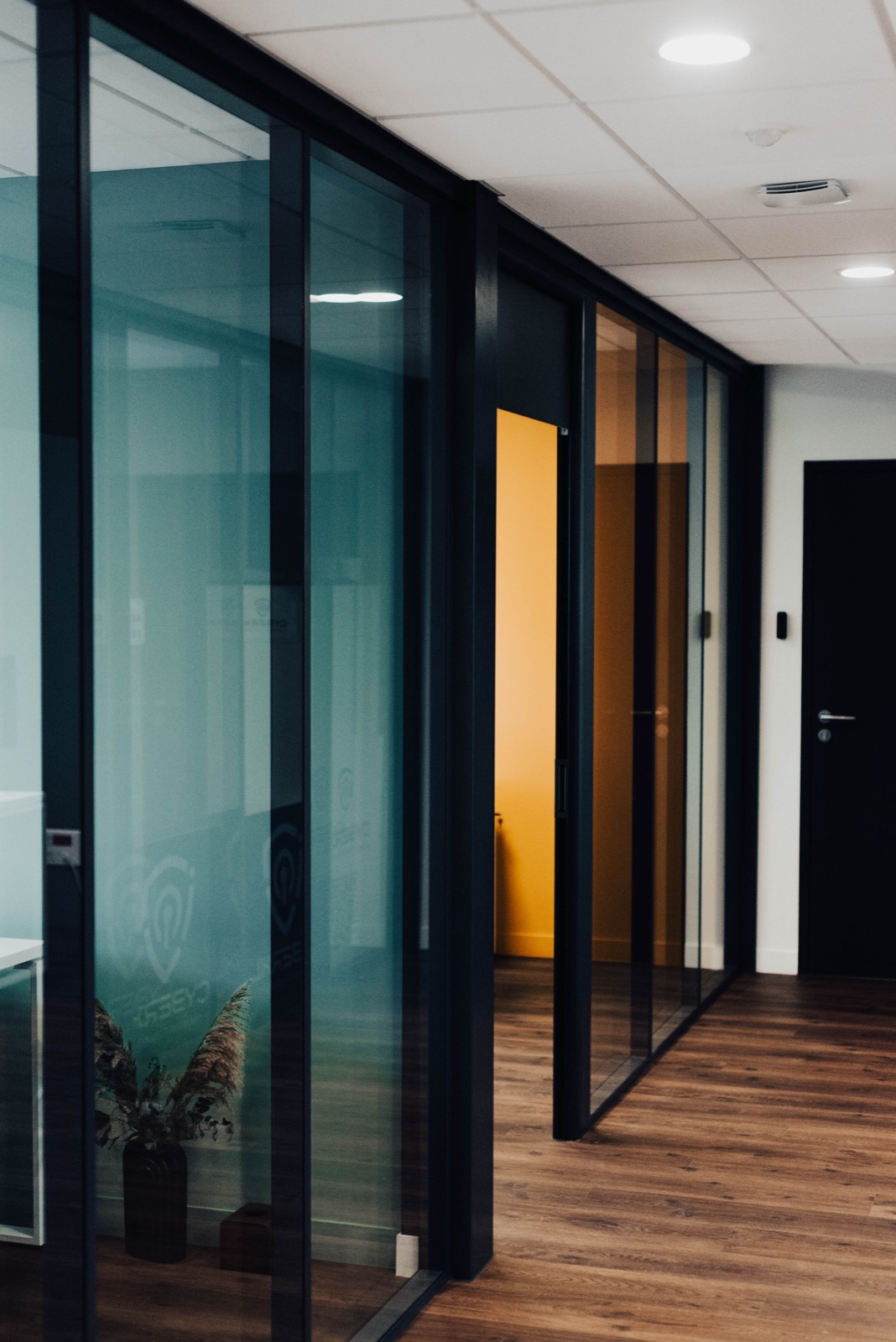 Circulation entre bureaux, lames PVC imitation bois et cloisons vitrées noires
